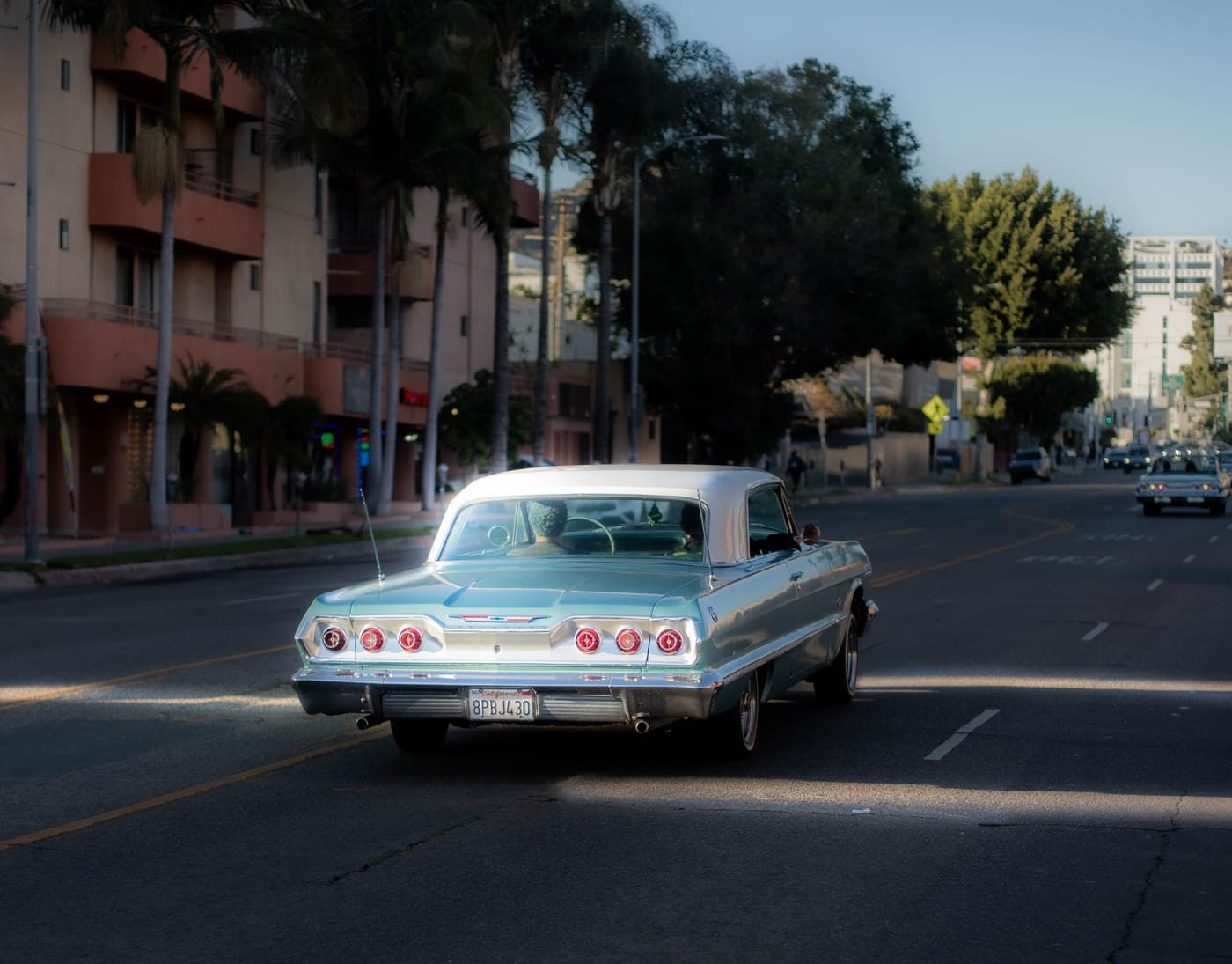Teal Chevrolet Impala rear view driving through LA palm-lined street