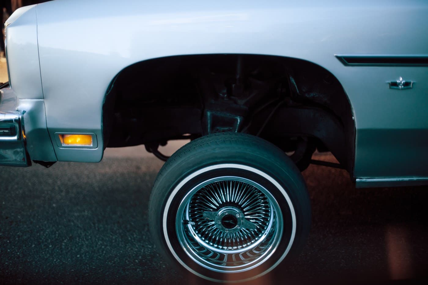 Teal lowrider Cadillac chrome wire wheel detail at night