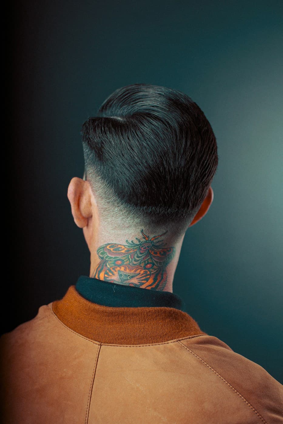 Back of head with neck tattoo and fade haircut, dramatic teal studio background