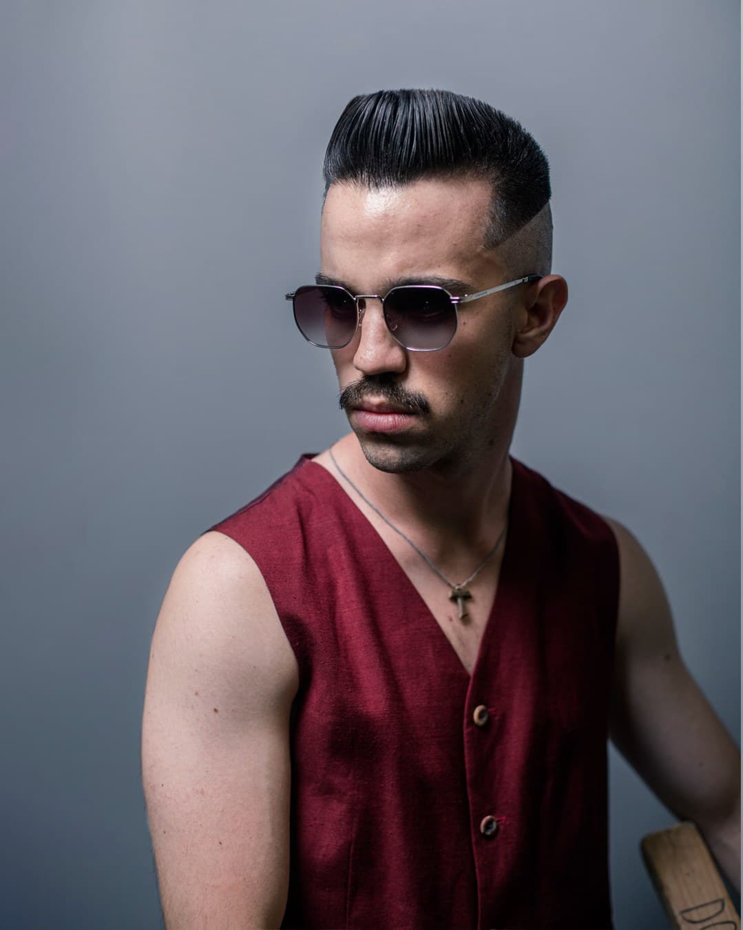Studio portrait, slicked side-part pompadour, burgundy vest and sunglasses