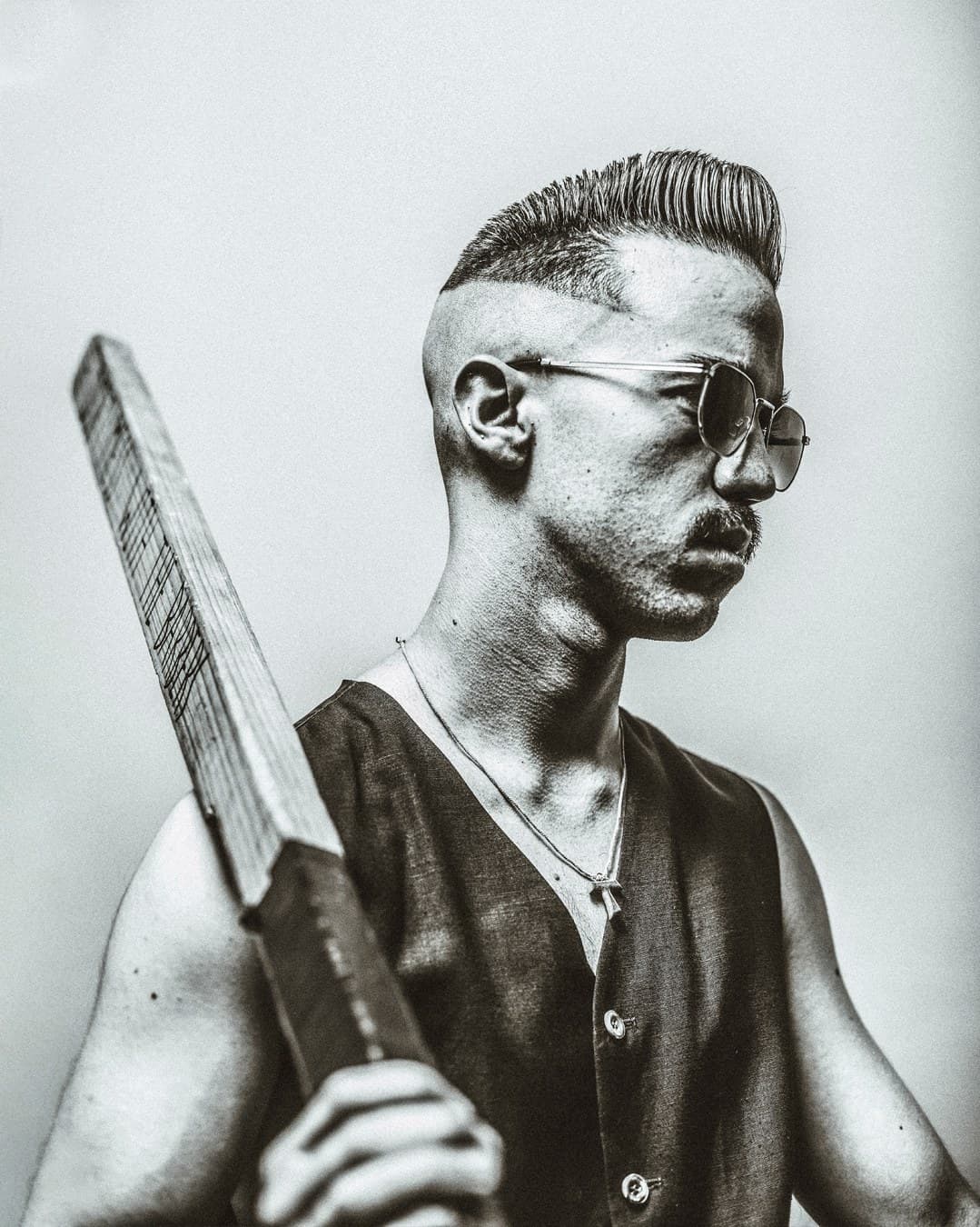 Black and white editorial — man with pompadour and straight razor, sunglasses
