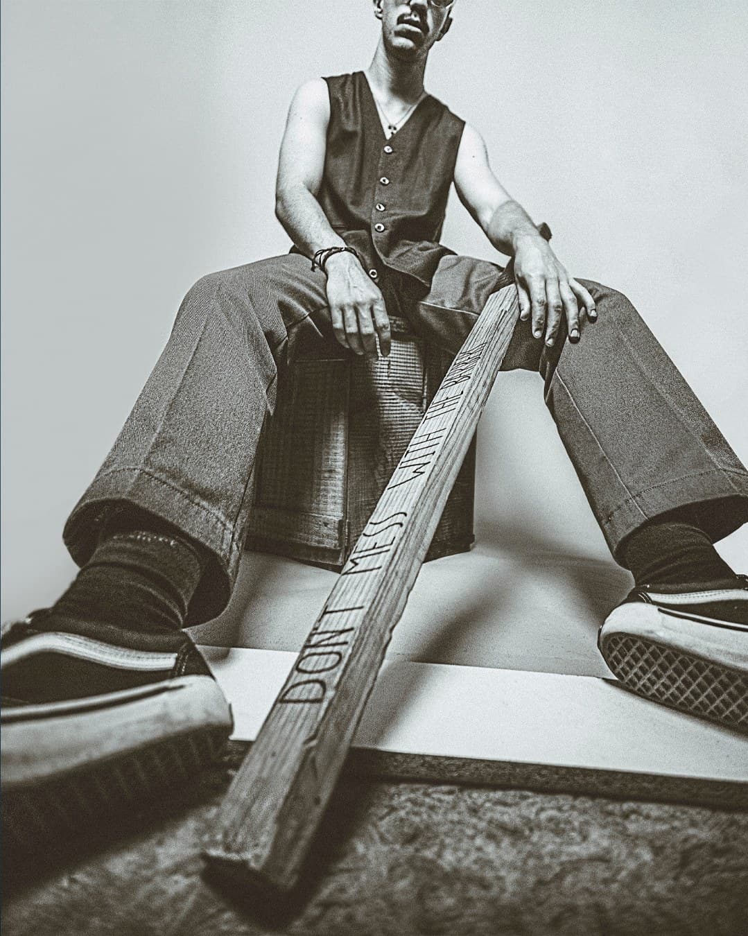 Black and white wide-angle editorial — man seated low with 'Don't Mess' bat