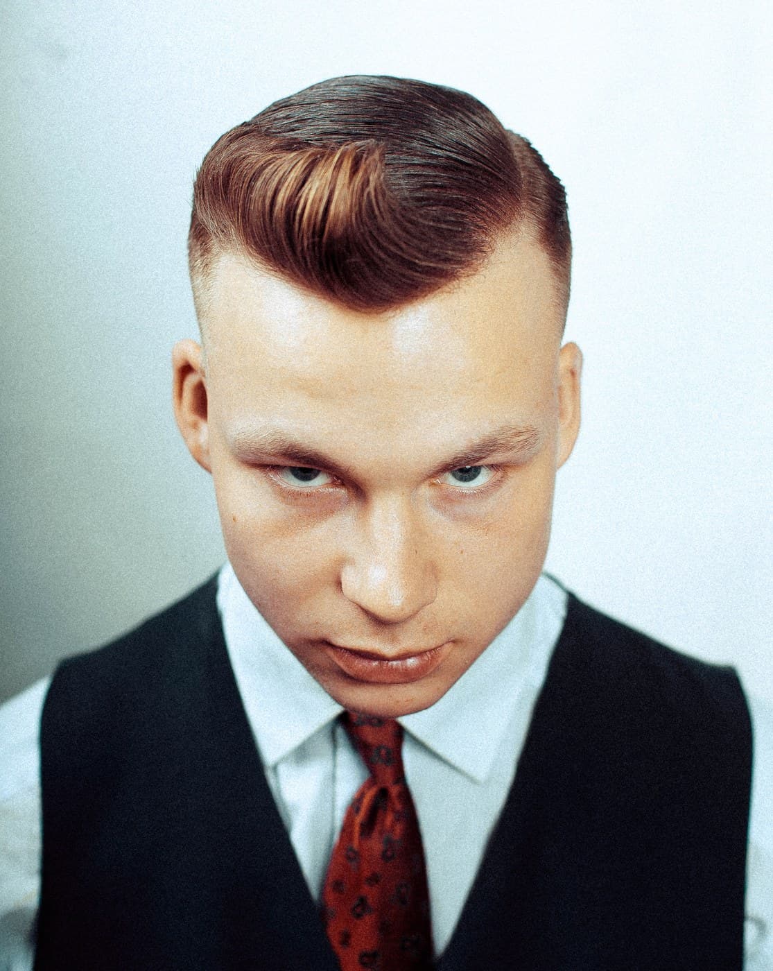Vintage-toned portrait — classic side-part pompadour, waistcoat and red tie