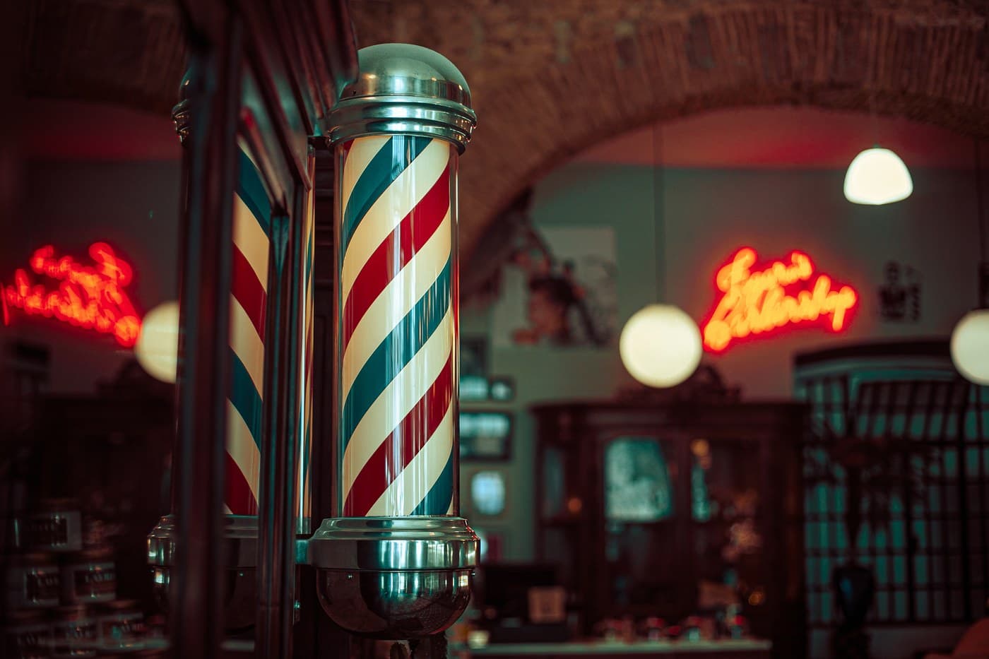 Classic red-white-blue barber pole with neon signs glowing in the background