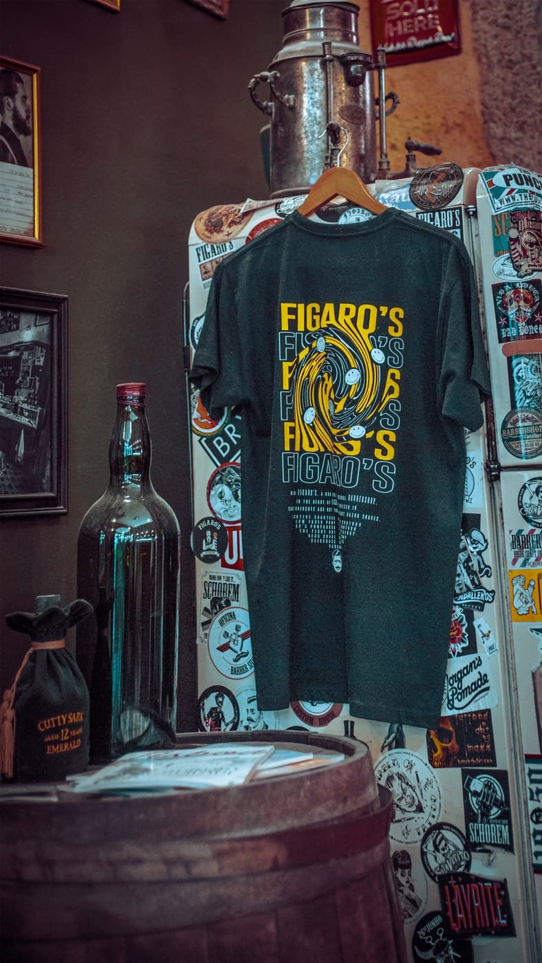 Figaro's branded t-shirt on hanger in front of sticker-covered vintage refrigerator