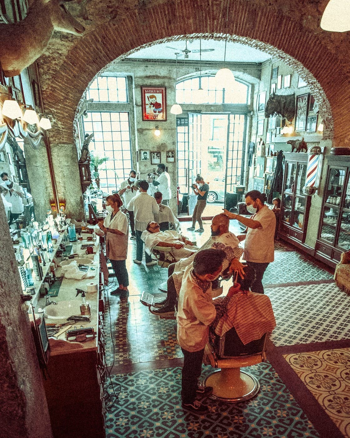 Barbershop interior framed through brick arch — barbers at work, full house