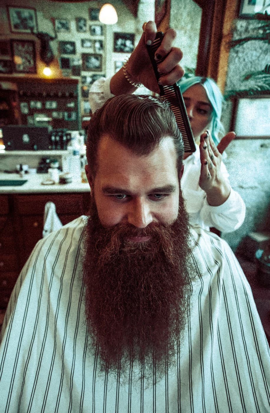 Barber with blue hair combs beard-frame pompadour, barbershop interior backdrop