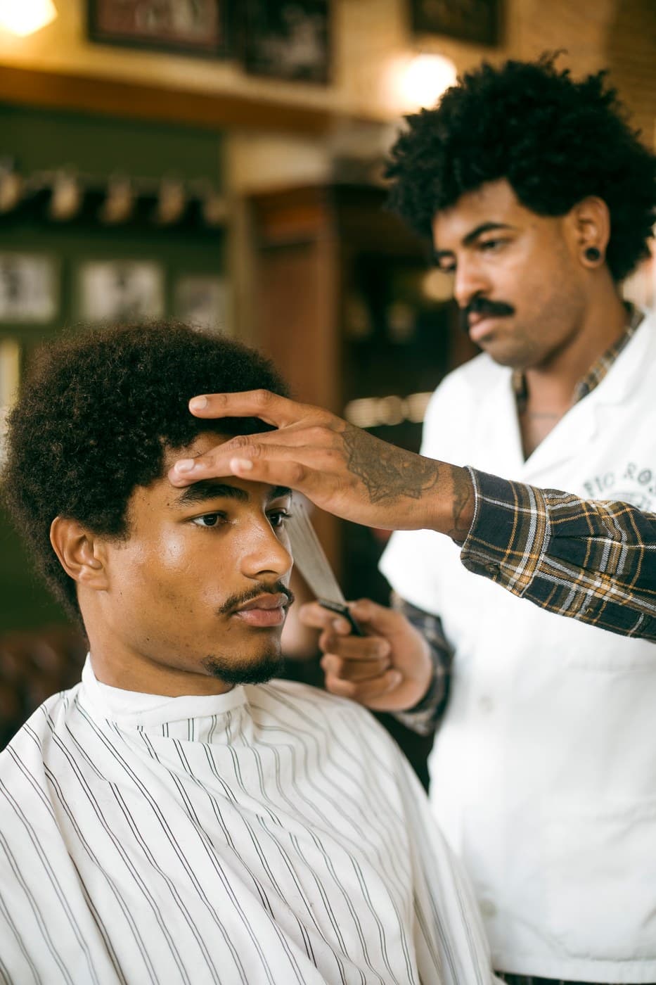 Barber with natural curls trims a client's afro, barbershop interior warm tones